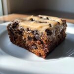 A close-up shot of a moist slice of banana bread brownies studded with chocolate chips and topped with a caramel-colored glaze.