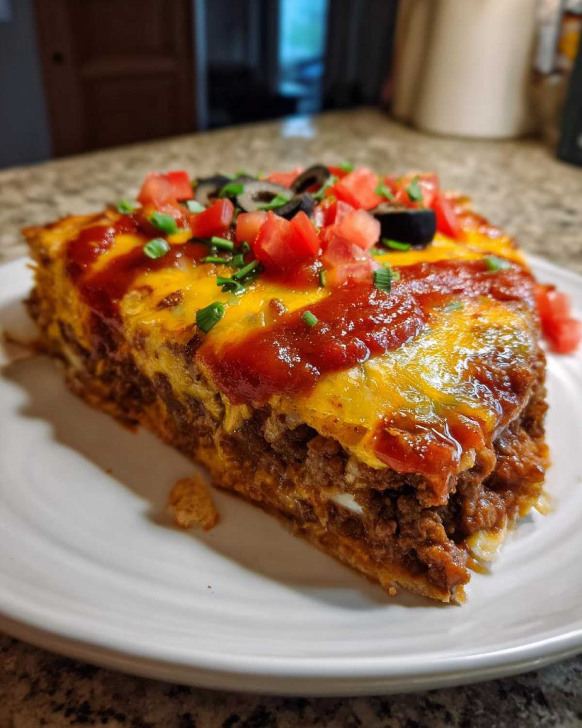 A thick slice of layered mexican pizza topped with melted cheese, salsa, diced tomatoes, olives, and green onions.
