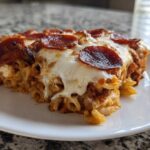 A generous slice of baked pizza casserole topped with melted mozzarella and crispy pepperoni on a white plate.