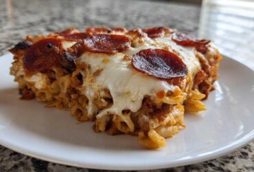 A generous slice of baked pizza casserole topped with melted mozzarella and crispy pepperoni on a white plate.