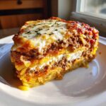 A thick, layered slice of spaghetti pie featuring pasta, rich meat sauce, and melted cheese topping.