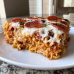 A generous slice of baked pizza casserole featuring pasta, tomato sauce, melted mozzarella, and pepperoni slices.