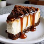 A thick slice of creamy salted caramel cheesecake drizzled with rich caramel sauce and topped with crumbs.