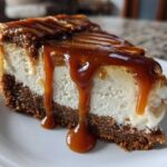 A decadent slice of salted caramel cheesecake with a thick graham cracker crust and rich caramel sauce dripping down the side.