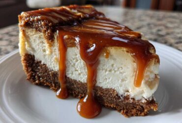 A decadent slice of salted caramel cheesecake with a thick graham cracker crust and rich caramel sauce dripping down the side.