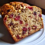 A close-up, appetizing slice of cranberry walnut bread showing dried cranberries and chopped walnuts embedded in the moist crumb.