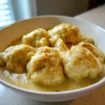 Close-up of fluffy dumplings smothered in creamy sauce from slow cooker chicken and dumplings in a white bowl.