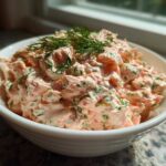 A close-up of a white bowl filled with creamy, chunky smoked salmon dip garnished with fresh dill.