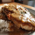 Close-up of a breaded chicken breast covered in rich brown gravy served alongside fluffy white rice, a perfect smothered chicken and rice dish.