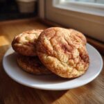 A stack of three soft, chewy snickerdoodles generously coated in cinnamon sugar, resting on a white plate.