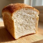 A loaf of soft sourdough sandwich bread cut in half, showing its fluffy white interior and golden crust.