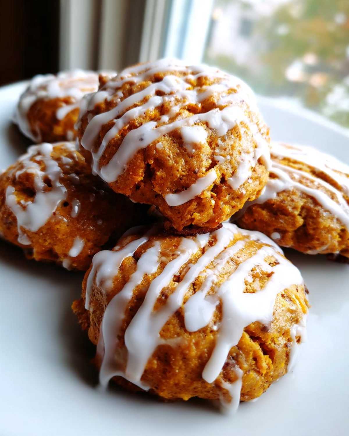 A stack of soft spiced persimmon cookies drizzled generously with white vanilla icing.
