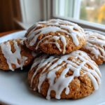 A stack of four soft spiced persimmon cookies drizzled generously with white vanilla icing on a white plate.