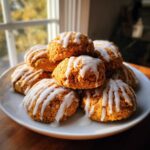 A stack of soft, spiced persimmon cookies drizzled generously with white vanilla glaze, set on a white plate.