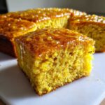 Close-up of a square slice of bright yellow sourdough cornbread topped with a glistening honey glaze.