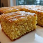 Close-up of a square slice of moist, yellow sourdough cornbread topped with a white glaze drizzle.