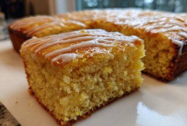 Close-up of a square slice of moist, yellow sourdough cornbread topped with a white glaze drizzle.