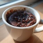 A close-up of a freshly baked, steaming chocolate mug cake topped with melted chocolate chips.