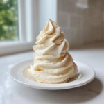 A tall, perfectly swirled serving of creamy banana ice cream on a small white plate.