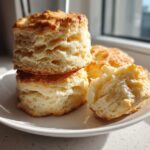 A stack of tall, golden-brown buttermilk biscuits showing off their flaky layers, served on a white plate.