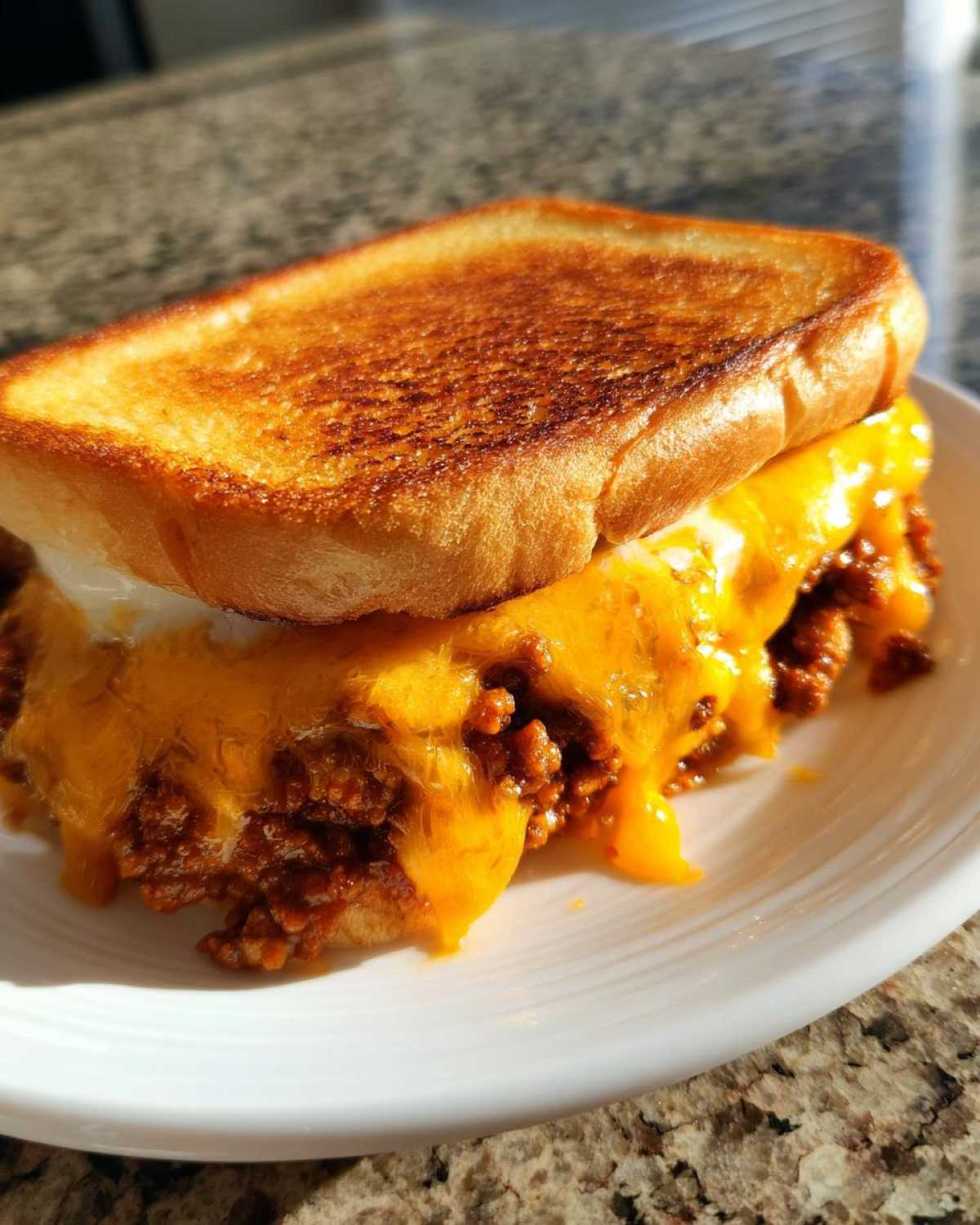 Close-up of a delicious texas toast sloppy joes sandwich with melted cheddar cheese overflowing onto a white plate.