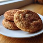 Three soft, chewy snickerdoodles heavily coated in cinnamon sugar resting on a small white plate.