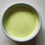 Overhead view of a bowl of bright green, velvety celery soup with a frothy top layer.