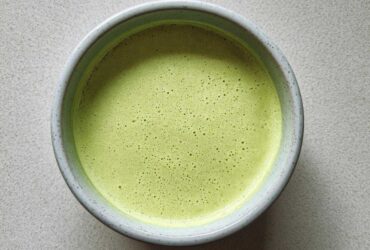 Overhead view of a bowl of bright green, velvety celery soup with a frothy top layer.