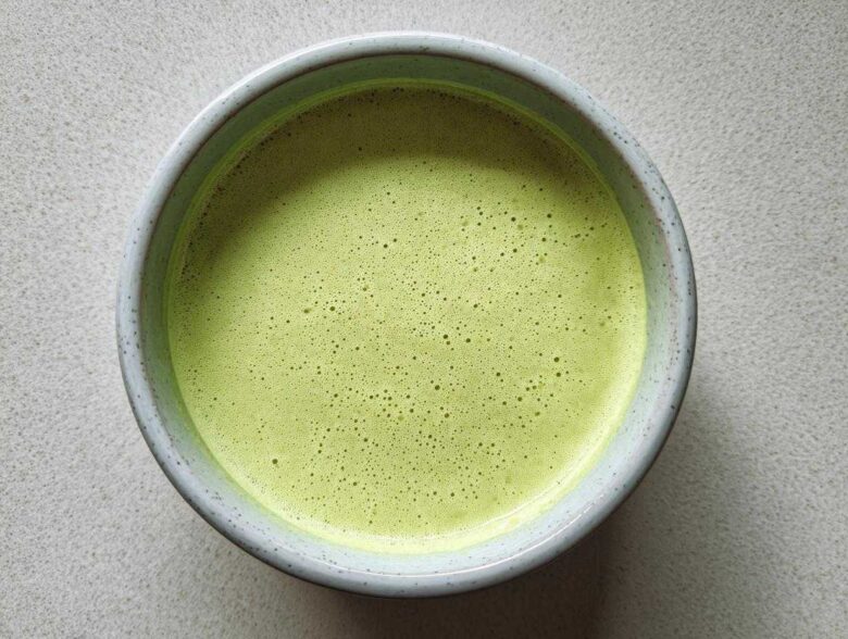 Overhead view of a bowl of bright green, velvety celery soup with a frothy top layer.
