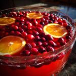 Close-up of a bright red thanksgiving punch garnished with floating whole cranberries and orange slices.