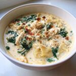 Close-up of a bowl of rich white chicken lasagna soup with shredded chicken, spinach, and pasta.