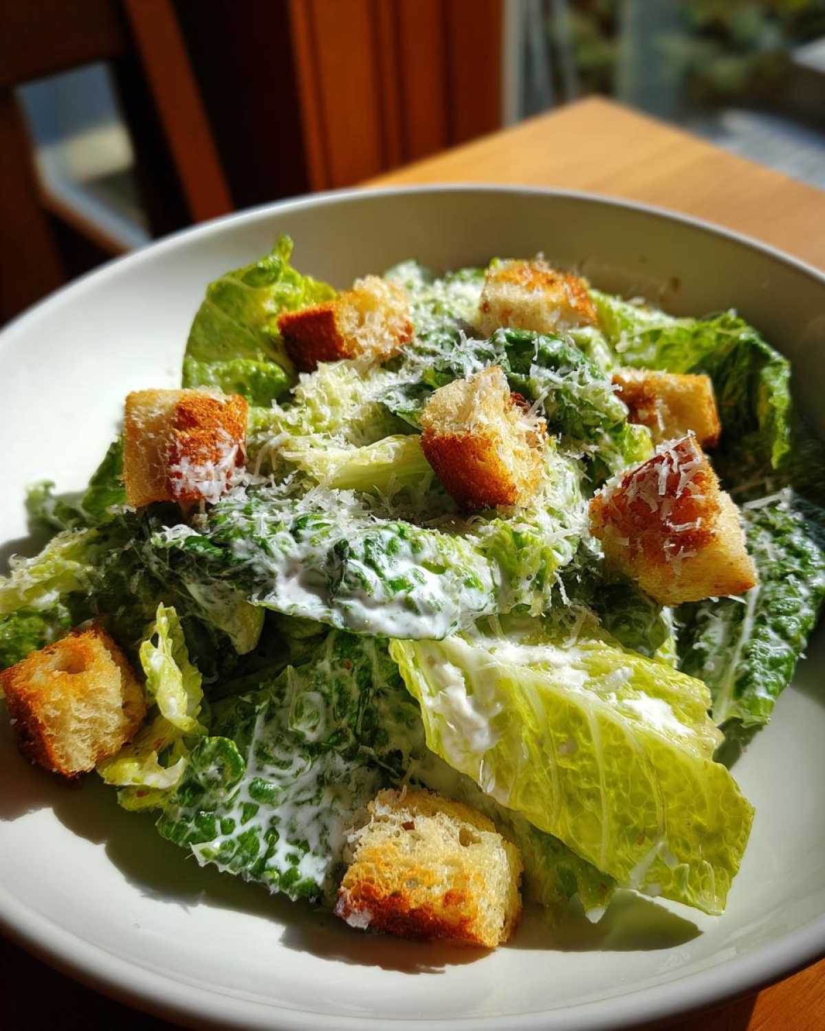 A close-up of a vibrant caesar salad featuring crisp romaine lettuce coated in creamy dressing, topped with golden croutons and grated Parmesan.