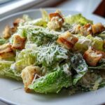 Close-up of a fresh Caesar salad featuring crisp romaine lettuce, creamy dressing, crunchy croutons, and grated Parmesan cheese.