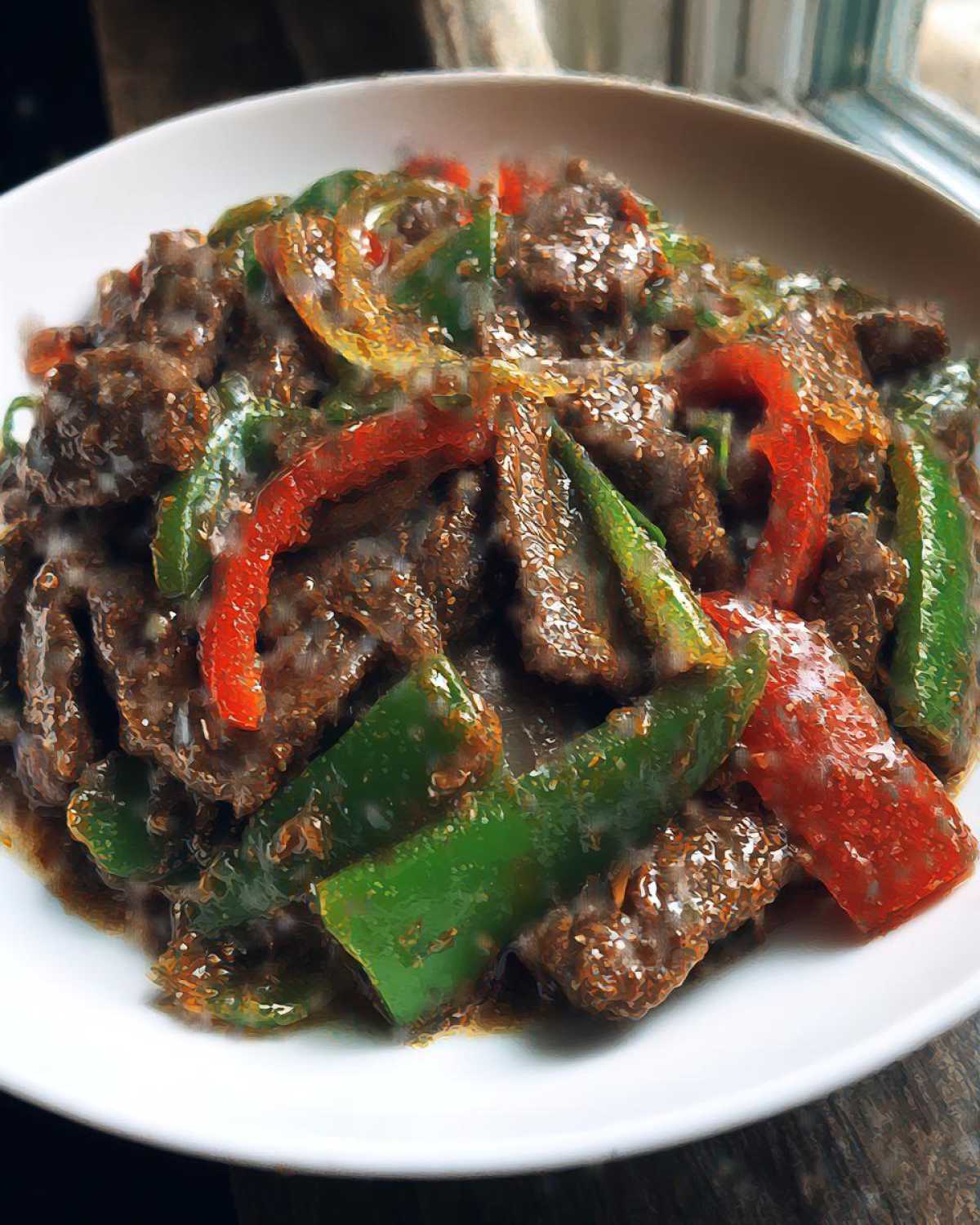 Close-up of savory pepper steak featuring strips of beef coated in sauce with vibrant green and red bell peppers.