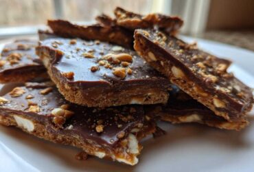 Close-up of stacked pieces of rich graham cracker toffee topped with melted chocolate and crushed nuts.