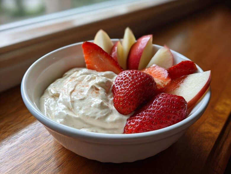 Close-up of a creamy fruit dip in a white bowl served with fresh strawberries and apple slices.