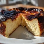 A whole basque cheesecake with a slice cut out, showing the creamy interior and signature dark, burnt top.