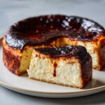 A slice of creamy basque cheesecake with a deeply caramelized, almost burnt top, next to the rest of the cake.