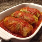 Three savory cabbage rolls covered in bright red tomato sauce, nestled in a white baking dish.