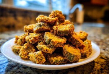 A close-up shot of a mound of perfectly crispy, golden-brown fried okra slices served on a white plate.