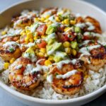 Close-up of a delicious shrimp bowl featuring grilled shrimp over white rice, topped with corn, avocado, tomato salsa, and a creamy drizzle.