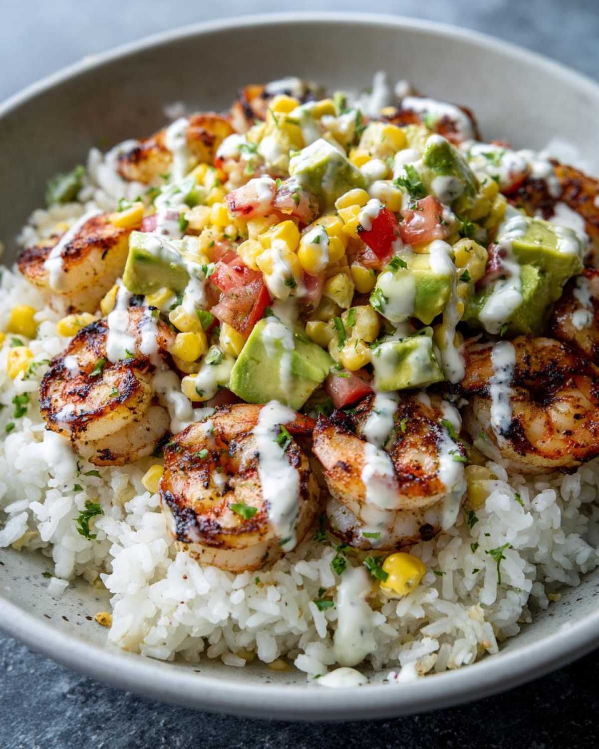Close-up of a delicious shrimp bowl featuring grilled shrimp over white rice, topped with corn salsa, avocado, and a creamy drizzle.