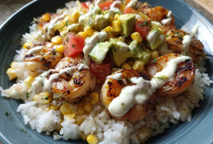 Close-up of a vibrant shrimp bowl featuring grilled shrimp, white rice, corn, avocado, tomatoes, and a creamy drizzle.