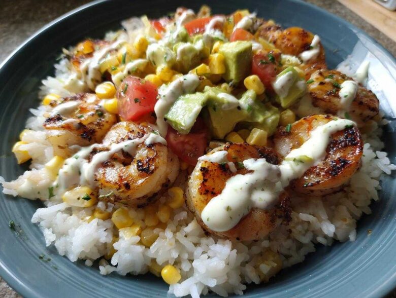 Close-up of a vibrant shrimp bowl featuring grilled shrimp, white rice, corn, avocado, tomatoes, and a creamy drizzle.