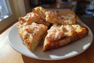 Four golden-brown slices of delicious shrimp toast topped with creamy shrimp mixture, served on a white plate.