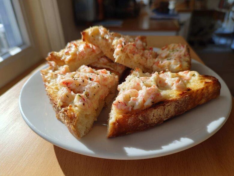 Four golden-brown slices of delicious shrimp toast topped with creamy shrimp mixture, served on a white plate.