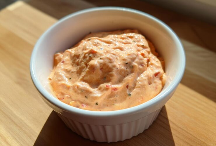 Close-up of creamy, orange-hued smash burger sauce speckled with herbs in a small white bowl.