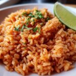 Close-up of a serving of bright orange Spanish rice garnished with fresh cilantro and a lime wedge.