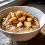 A close-up of creamy apple cinnamon oatmeal topped with diced, cinnamon-dusted apples in a white bowl.