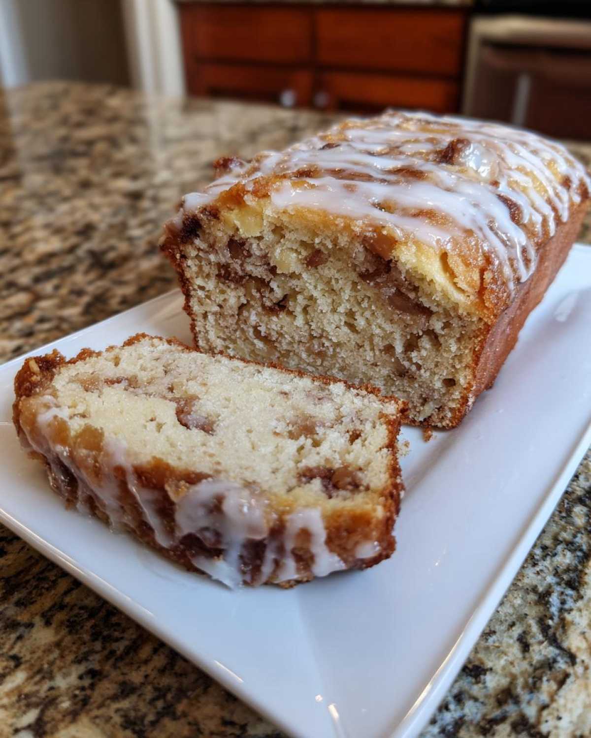 A loaf of sweet apple fritter bread with a slice cut, drizzled with white icing.